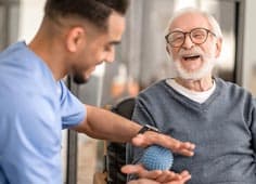 Male Nurse Conducting Hand Therapy On Elderly Man With Ball