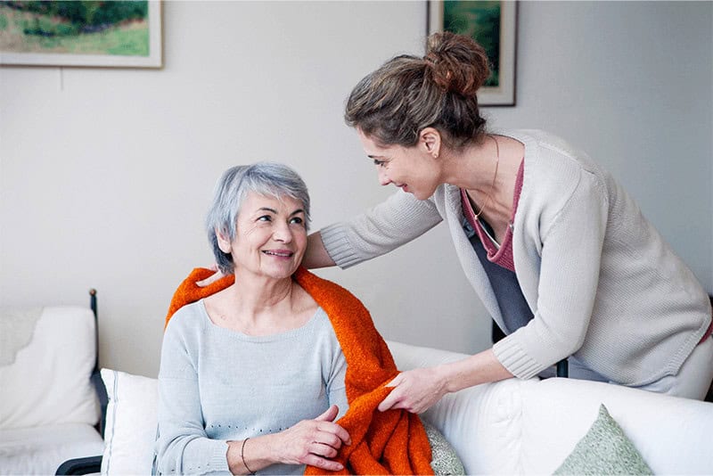 female home health aide placing a blanket on a senior woman