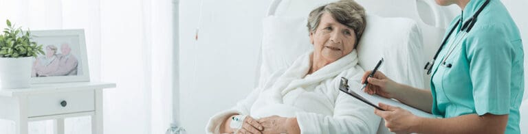 nurse with a clipboard talking to an elderly woman in a hospital bed